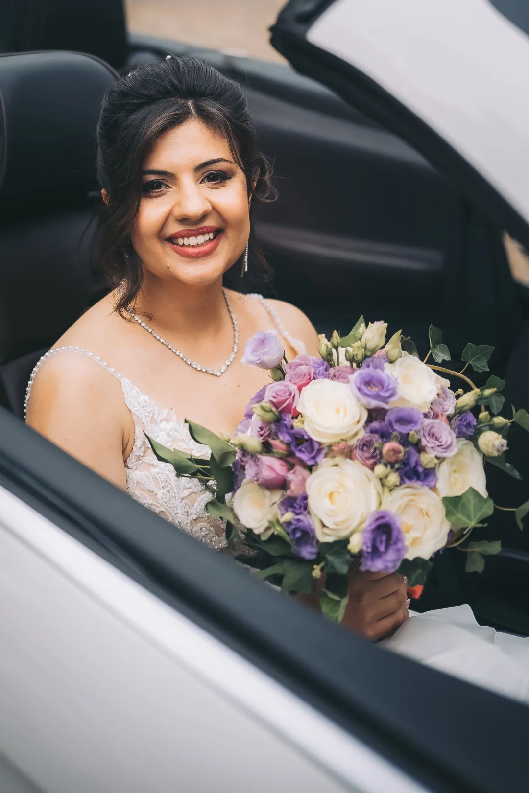 hochzeitsfotograf-wolfsburg-braut-im-cabrio Eine lächelnde Braut sitzt in einem weißen Cabrio und hält einen Brautstrauß in der Hand
