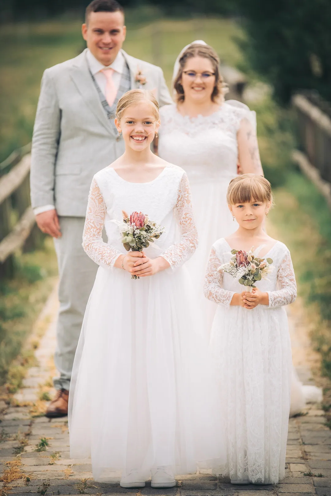 hochzeitsfotograf-wolfsburg-familie Eine Familie posiert am Tag der Hochzeit, im Vordergrund sind zwei Mädchen in weißen Kleidern mit Blumen in den Händen zu sehen, im Hintergrund steht das glückliche Brautpaar