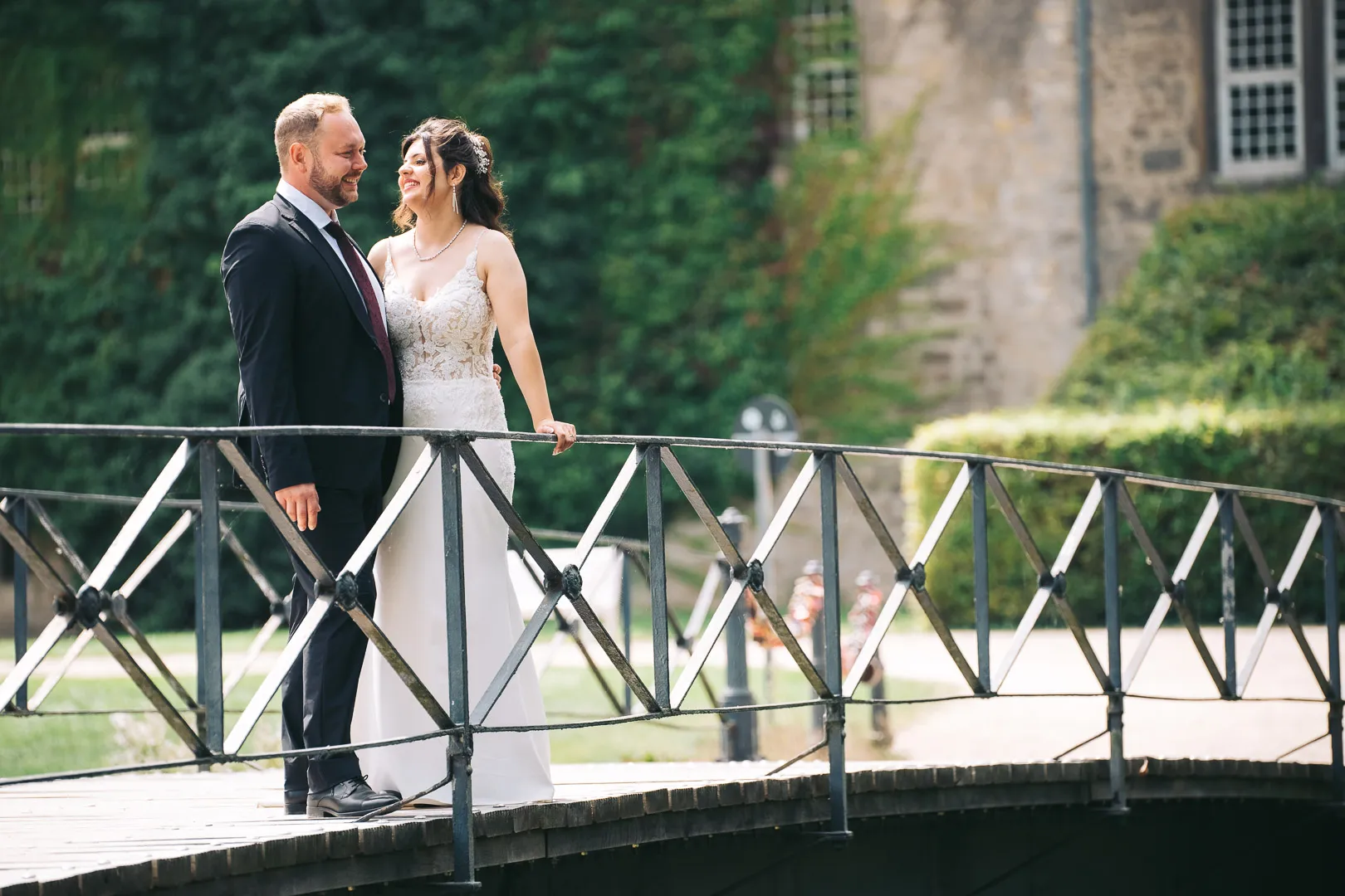 hochzeitsfotograf-wolfsburg-hochzeitspaar-auf-bruecke Ein Brautpaar steht auf der Brücke vor dem Schloss Wolfsburg, sie strahlt ihn an während er glücklich in die Ferne schaut