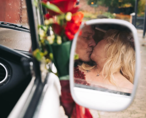 hochzeitsfotograf-wolfsburg-kuss-seitenspiegel Im Außenspiegel eines VW T1 Bus ist ein Brautpaar zu sehen, das sich küsst