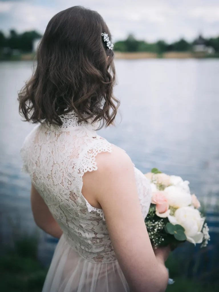Eine Braut ist während eines Fotoshootings am Mühlensee in Gifhorn von hinten zu sehen, sie trägt ein weißes Kleid mit Spitze und einen Brautstrauss.
