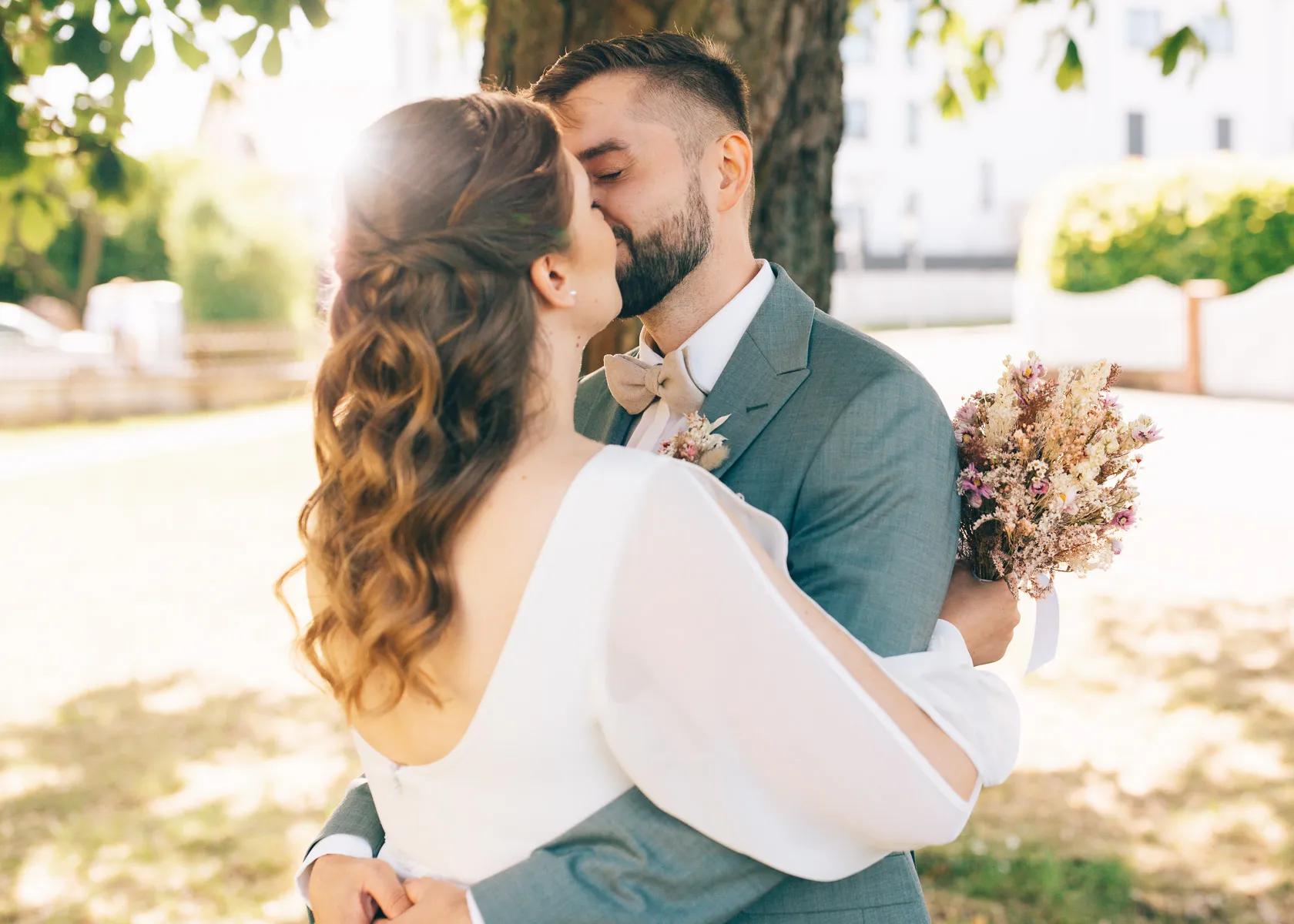 Ein Brautpaar küsst sich bei einer Hochzeit in Wolfsburg unter einem Baum.