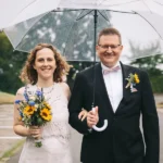 Brautpaar Maren und Dennis spaziert mit einem Regenschirm über dem Parkplatz am Theater Wolfsburg